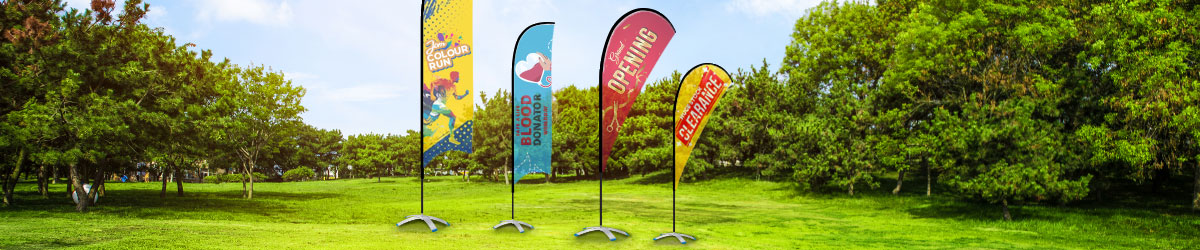 A lineup of  4 wind flag displaying different style, sizes and matched with different design: stock clearance, running events, blood donation and grand opening styled with matching scenes on a green garden