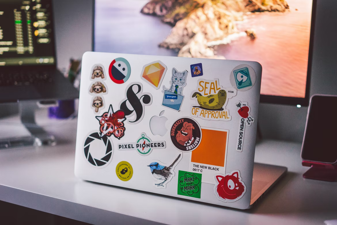 A silver Macbook on an office table covered in a variety of colorful stickers.