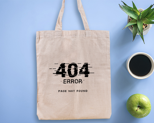 A white canvas tote bag is placed flat on a grey wooden surface, printed with a design in black that says Go Green with illustrations of plants, clouds, and other items. Nearby is a pile of fresh produce.
