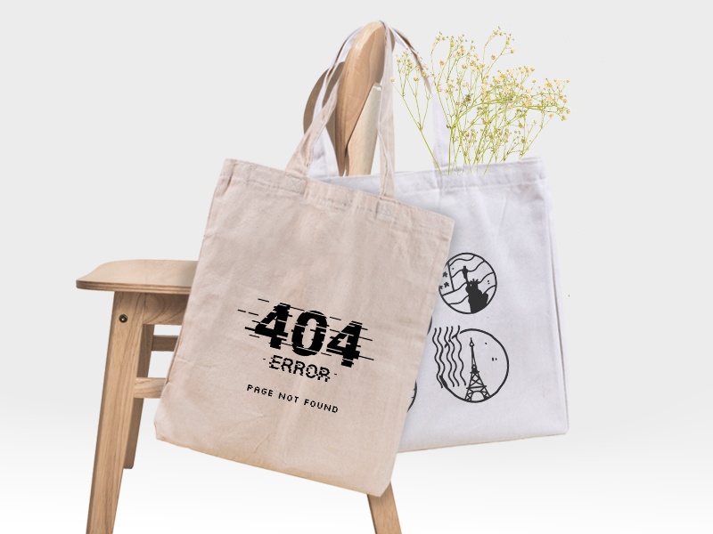 Two tote bags stand next to each other on a wooden surface against a blue background. One is tall and made of raw canvas, another is wide and of white canvas. Both have designs printed in black