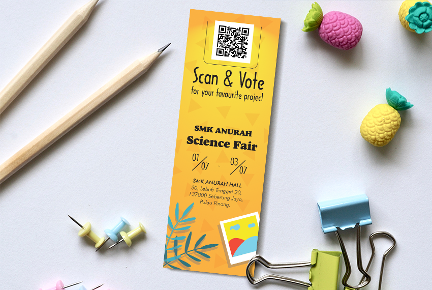 A yellow bookmark featuring a QR code and labelled “Scan & Vote”, placed on a white surface surrounded by an assortment of stationery.
