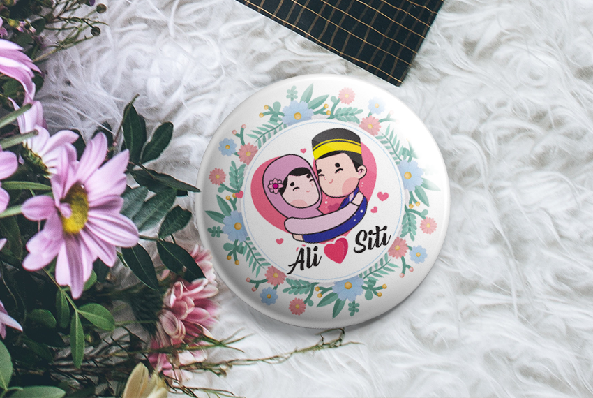 Button badge showing a cartoon couple surrounded by a floral border, and labelled “Ali ❤ Siti”, resting on a furry background next to a bouquet.