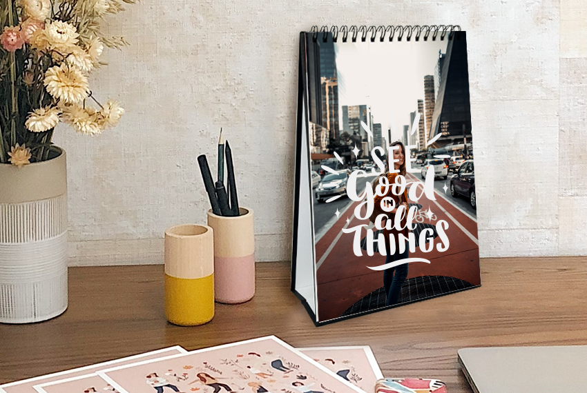 A hard stand desk calendar featuring an image of a person running through a city, the words “See Good in All Things” printed in large white text over the image.