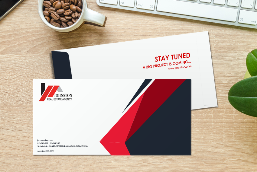 Two envelopes with a navy and red design rest atop one another on a wooden desk next to a cup full of coffee beans.