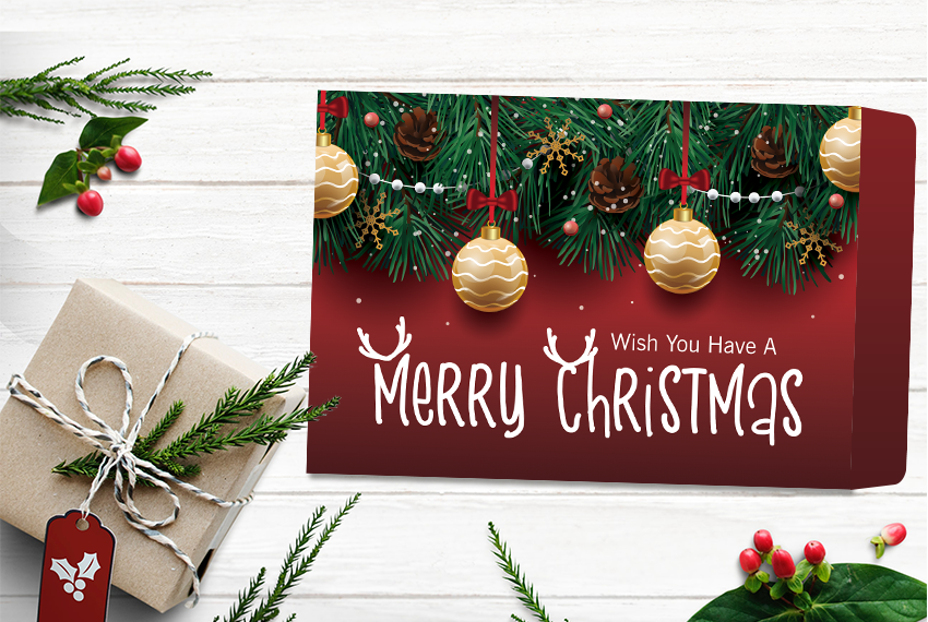 An envelope printed with a Christmas motif decorated with pine leaves on the top hung with baubles and pine cones, and the quote “Wish You Have A Merry Christmas” in white across the bottom on a red background.