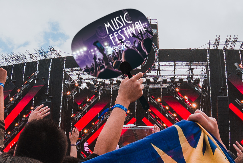 A person is holding aloft a hand fan at a concert surrounded by many people. The hand fan features an image of another concert with the words “Music Festival” printed on it.
