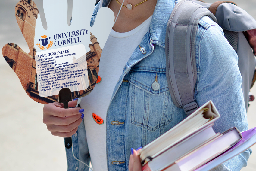 A woman in a denim jacket holds a simple hand-shaped fan printed with the text “University Cornell” and other text advertising a new intake.