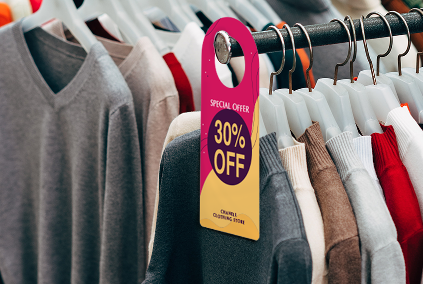 A pink and yellow hanger hangs on the edge of a rack of clothing, advertising that the rack is now “30% off”.