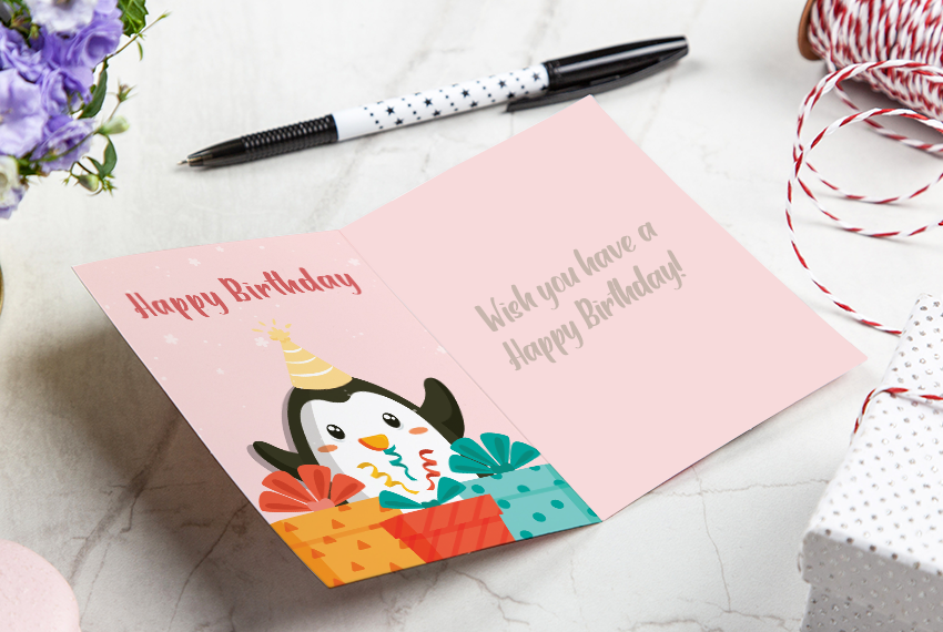 A greeting card wishing someone Happy Birthday and featuring a cartoon penguin sits on a white surface.