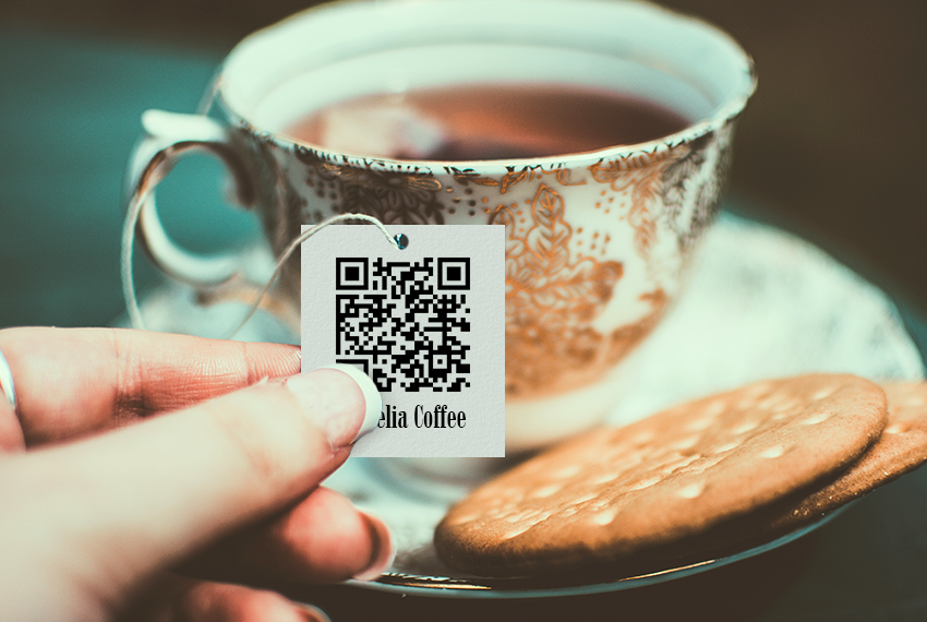 A hand holds a card printed with a QR code attached to a tea bag.