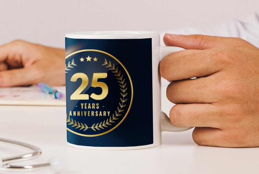 A hand holding a mug printed with the words “25 years anniversary” in gold text against a dark background.