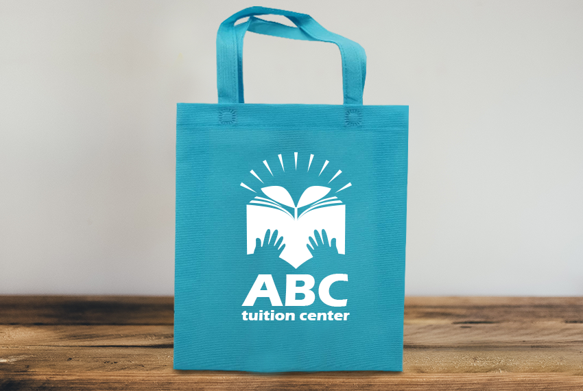 A blue tote bag printed with “ABC Tuition Centre” sits on a wooden surface.