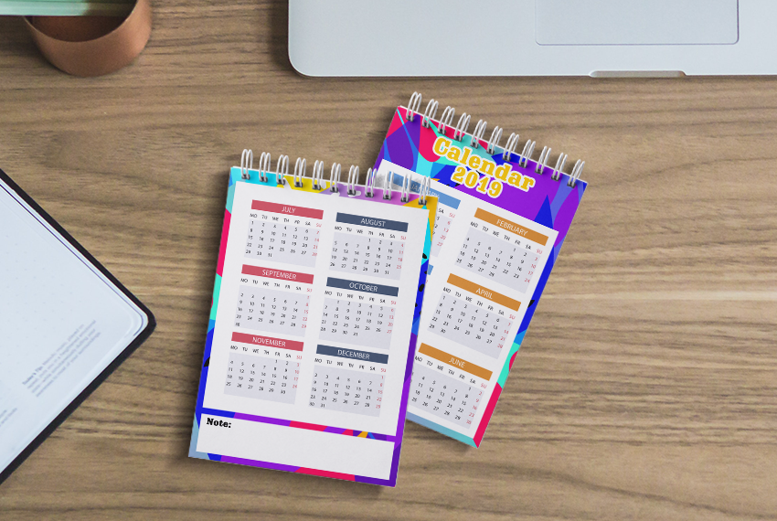Two wirebound notebooks are arranged side by side on a wooden surface, both featuring calendars.