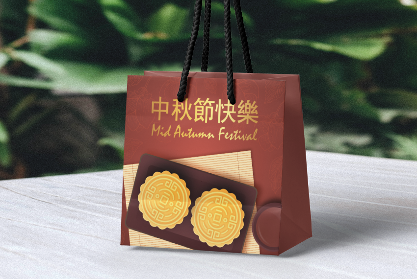 A paper bag featuring an image of mooncakes and text highlighting the Mid-Autumn Festival sits on a wooden surface.