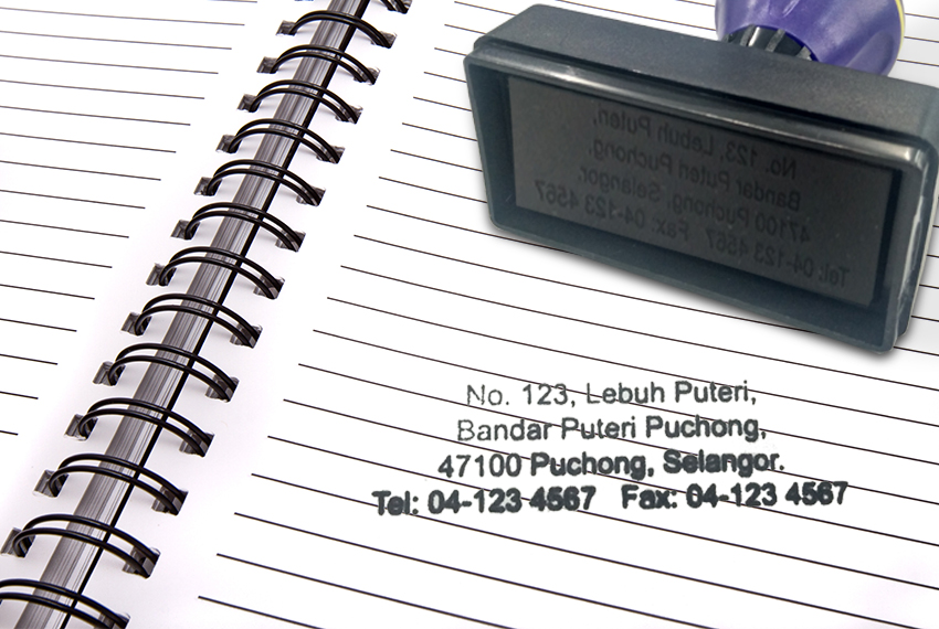 A rubber stamp with a blue handle next to a notebook that has been stamped with an address.