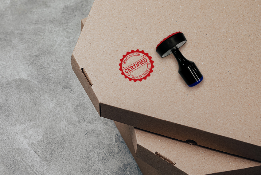 A rubber stamp that says “Certified” with a black handle rests on top of a stack of boxes.