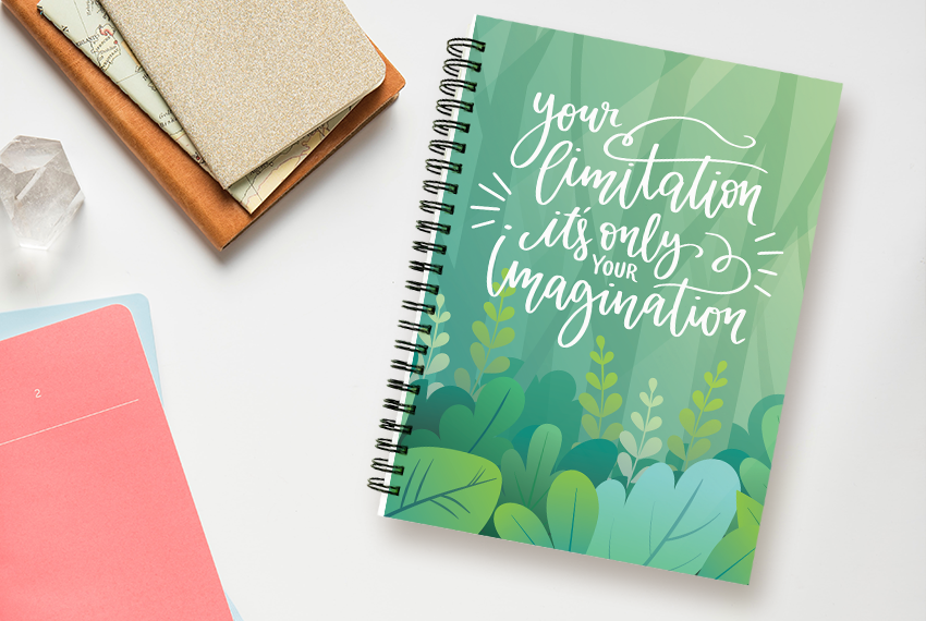 A green, wirebound notebook printed with a quote saying “Your limitation is only your imagination” sits next to a pile of stationery.